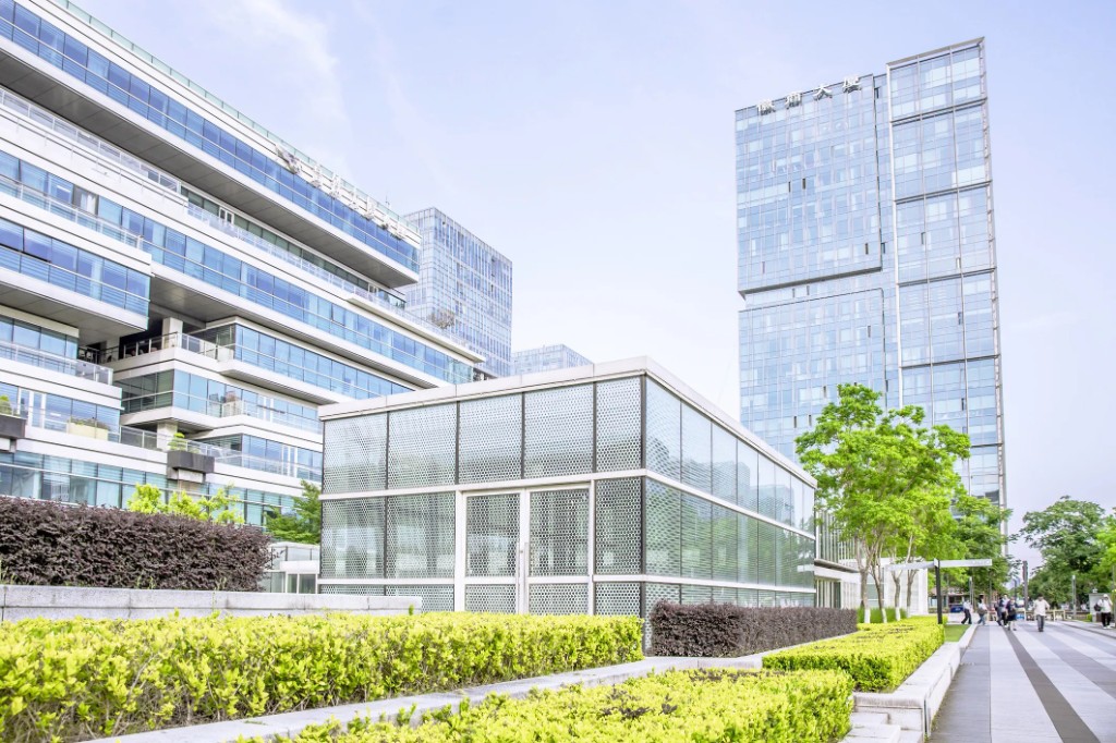 Modern glass-fronted commercial towers and a low pavilion under a clear sky, with manicured landscaping and a wide pedestrian plaza.