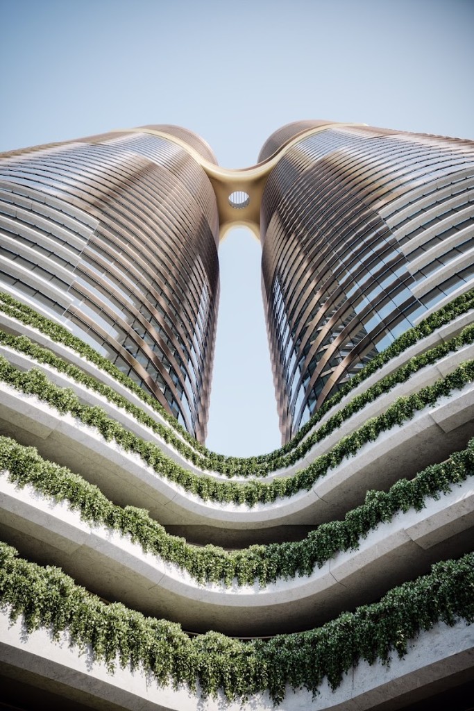 Modern sustainable towers with curved skybridge and lush greenery on terraced balconies against a clear sky.